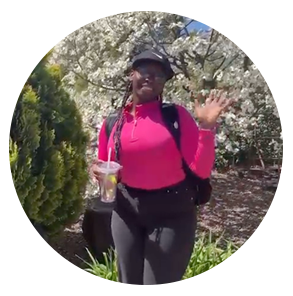 Nyasha站在一棵开花的树前，开心地对着镜头挥手
